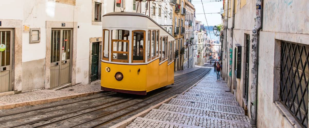 Bonde amarelo em rua inclinada cercada por pr&eacute;dios antigos.