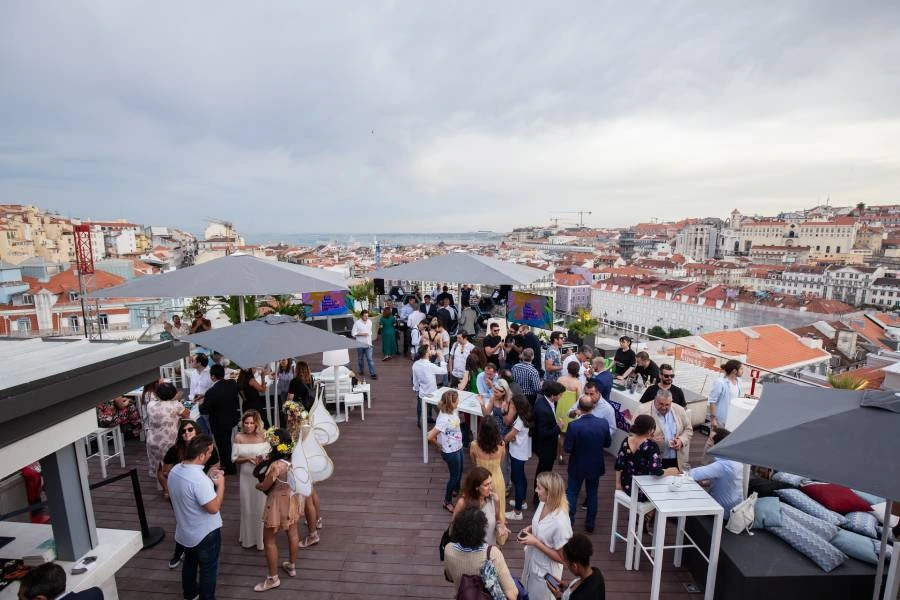 Grupo de pessoas em uma festa no terra&ccedil;o, com vista para a cidade ao fundo.