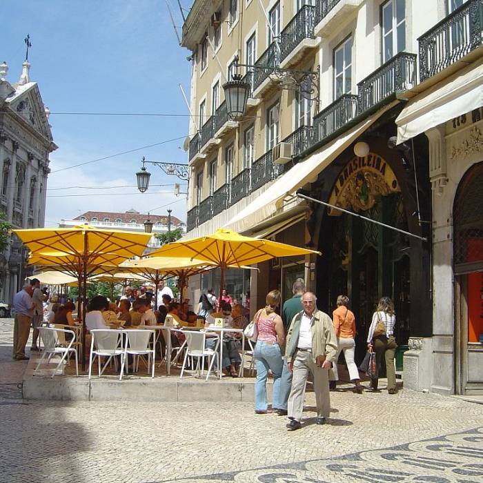 Cal&ccedil;ada movimentada com mesas e guarda-s&oacute;is amarelos ao ar livre.