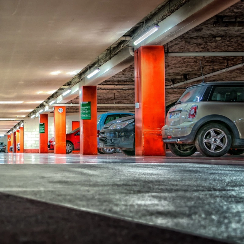 Estacionamento subterr&acirc;neo com carros entre colunas vermelhas.