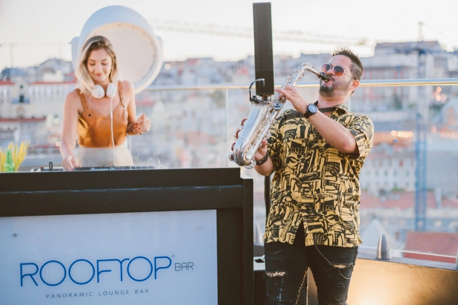 DJ e saxofonista em um rooftop, com cidade ao fundo.