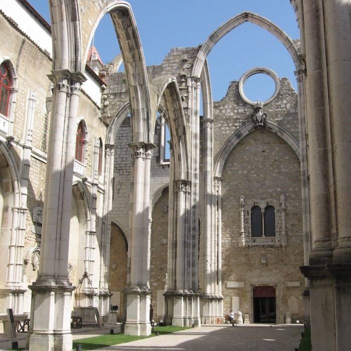 Ru&iacute;nas de um convento com arcos g&oacute;ticos contra um c&eacute;u azul.