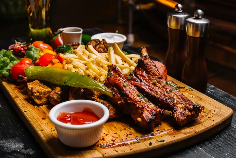 Tabla de madera con costillas, papas fritas y vegetales asados.