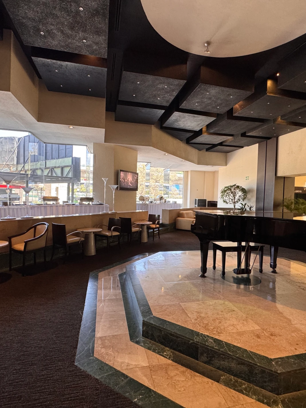 Vestíbulo con piano negro, techo geométrico y ventanas amplias.