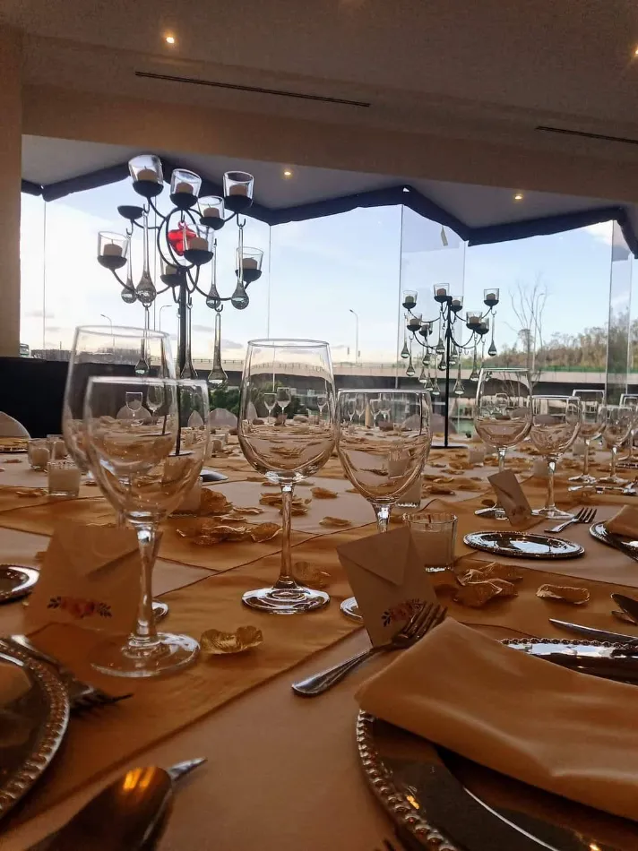 Mesa elegante con copas, platos y cubiertos en un sal&oacute;n iluminado.