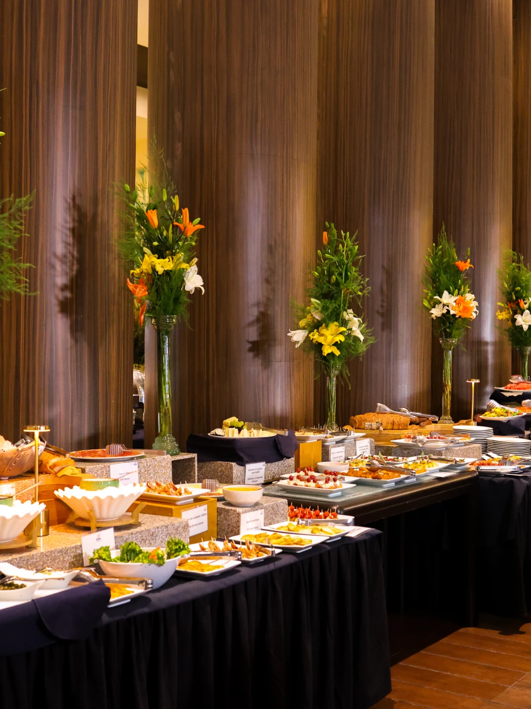 Mesa de buffet elegante con flores y varios platos variados y coloridos.