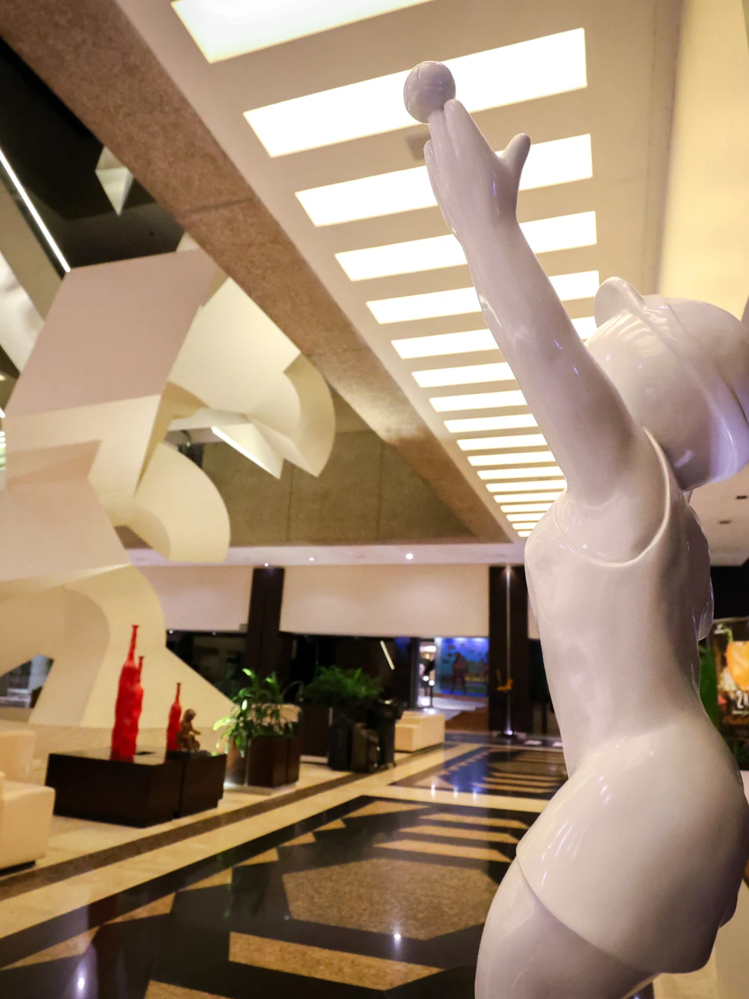 Una estatua blanca de un ni&ntilde;o lanzando una pelota en un vest&iacute;bulo elegante.