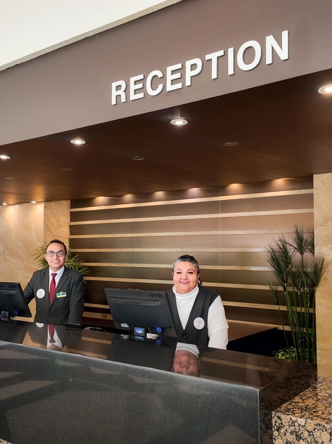 Recepcionistas sonrientes detr&aacute;s del mostrador de recepci&oacute;n de un hotel.