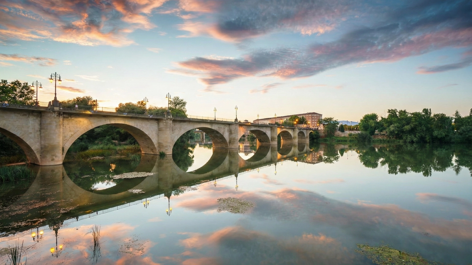 Un puente medieval con arcos reflejado en el r&iacute;o al atardecer.