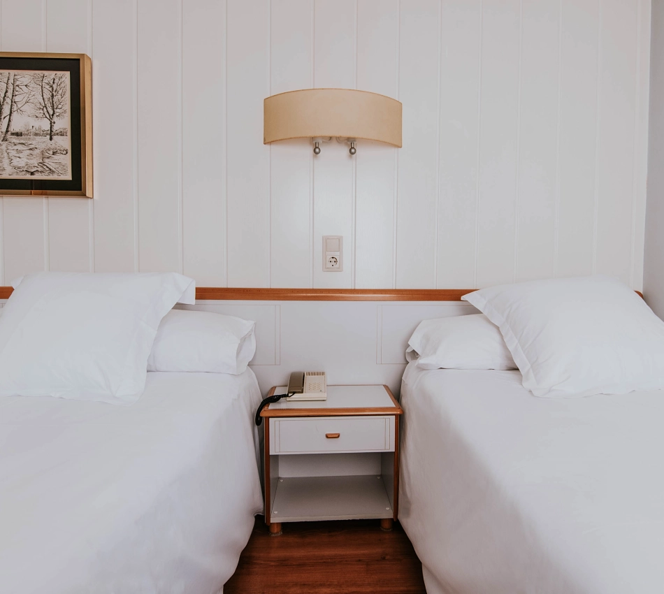 Dos camas individuales con mesa de noche en habitaci&oacute;n sencilla.