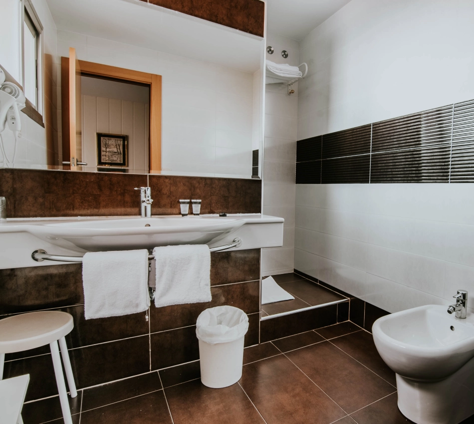 Ba&ntilde;o moderno con lavabo, botiqu&iacute;n, bid&eacute; y toallas blancas.