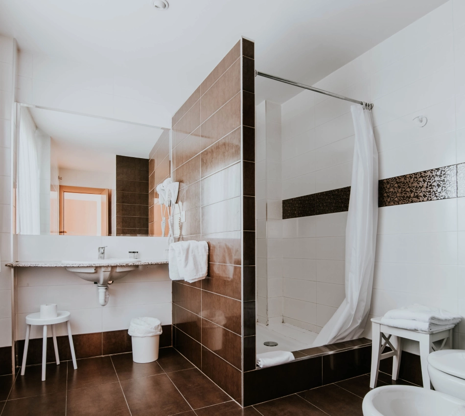 Ba&ntilde;o moderno con duchas, espejo, toallas blancas y detalles en marr&oacute;n.