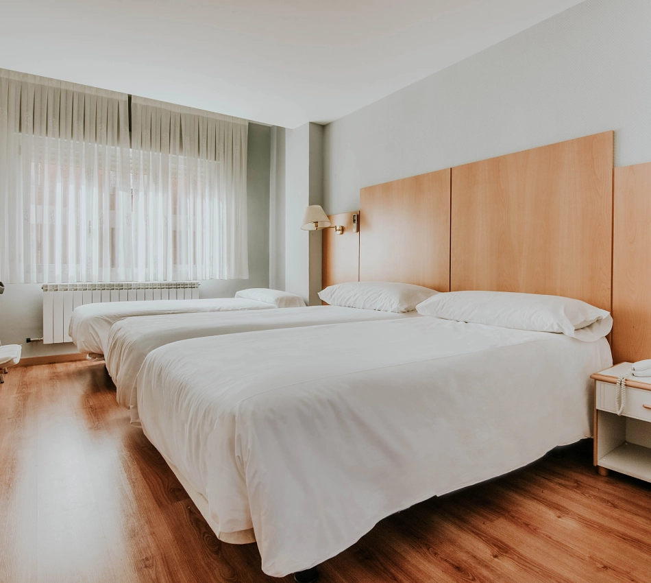 Habitaci&oacute;n con tres camas individuales, luz natural y suelo de madera.