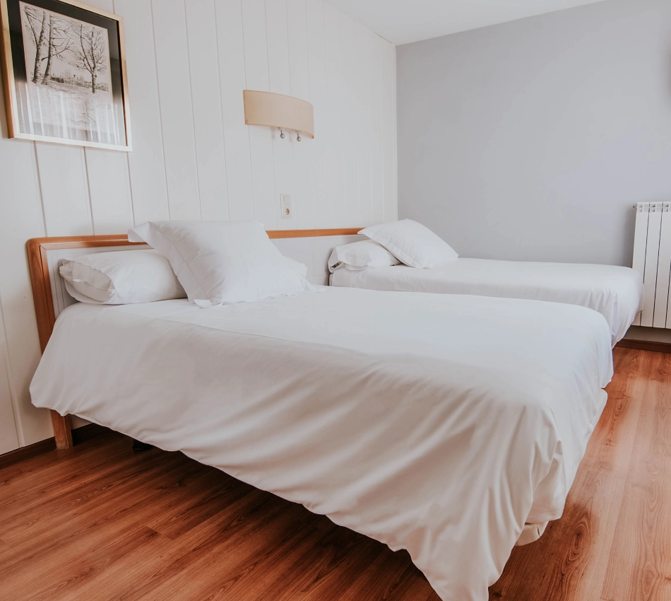 Dos camas individuales con ropa blanca en una habitaci&oacute;n minimalista.