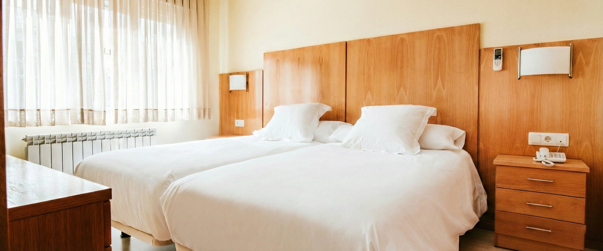 Habitaci&oacute;n de hotel con dos camas blancas y muebles de madera clara.