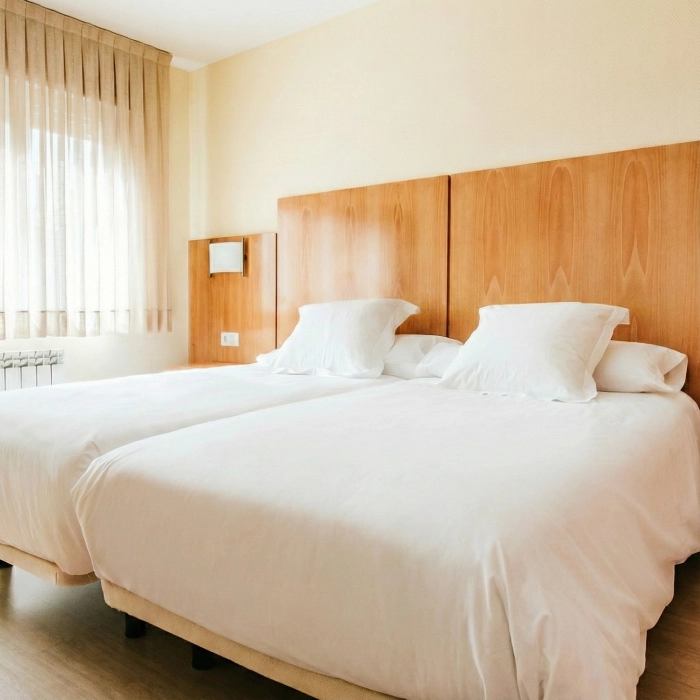 Habitaci&oacute;n con dos camas individuales, s&aacute;banas blancas y cabeceras de madera.