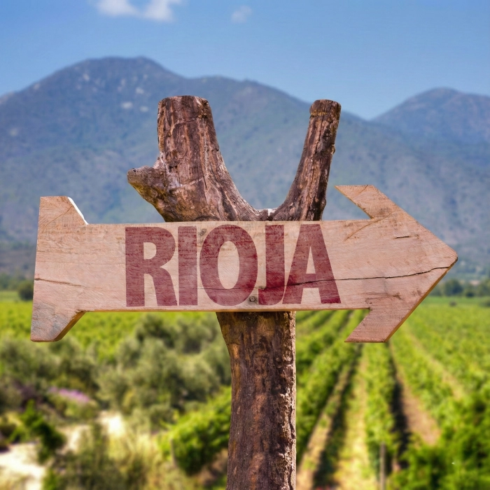 Se&ntilde;al de madera que dice "Rioja" con vi&ntilde;edos y monta&ntilde;as al fondo.