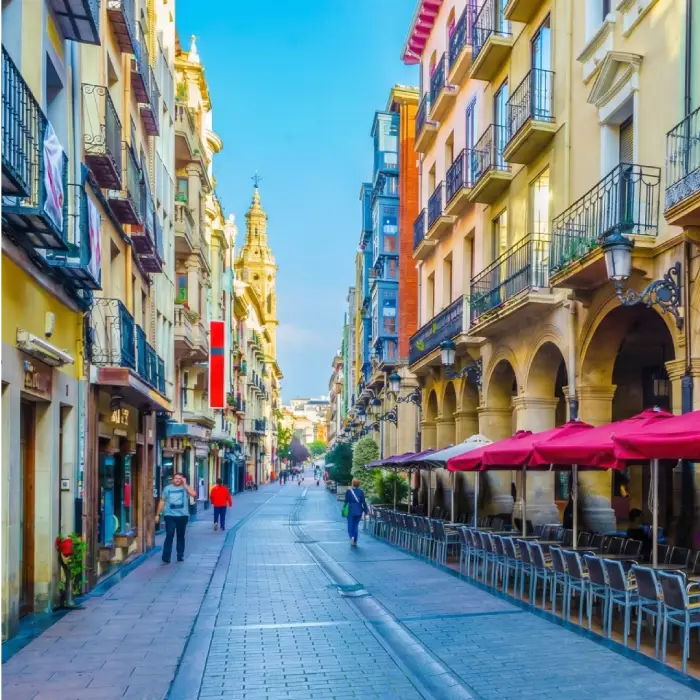 Calle estrecha con edificios coloridos y caf&eacute;s al aire libre en un d&iacute;a soleado.