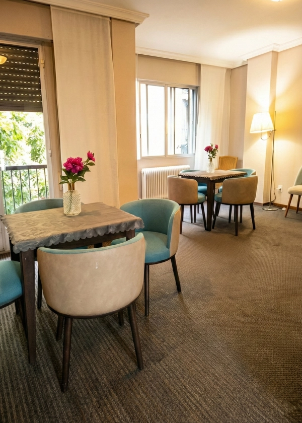 Sala con varias mesas, sillas tapizadas y jarrones con flores rosadas.