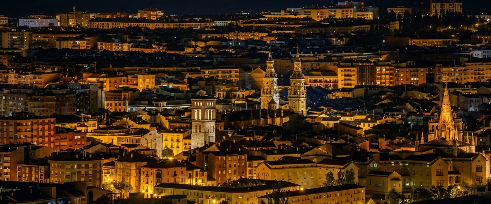 Vista nocturna de una ciudad iluminada con edificios y una iglesia destacada.