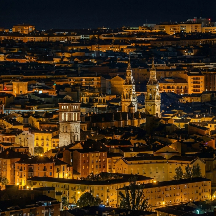 Ciudad iluminada de noche con torres de iglesia destacadas.