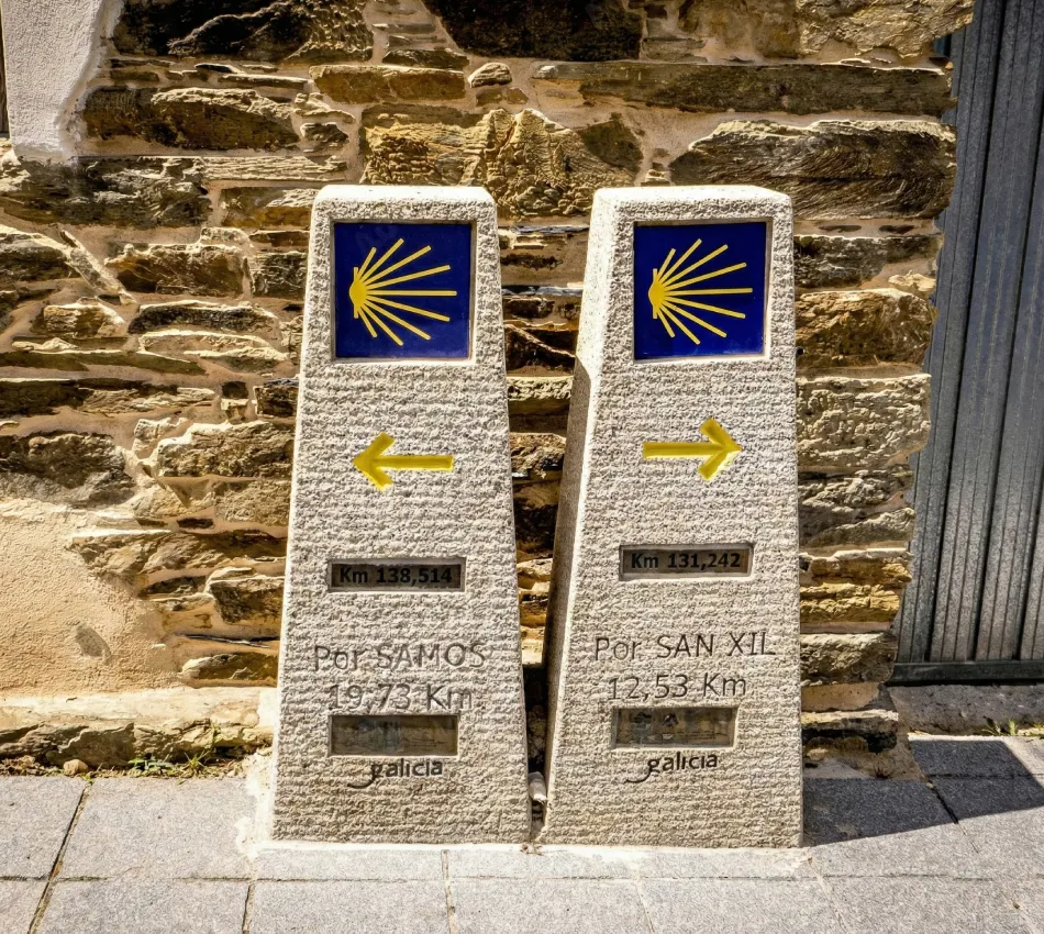 Dos mojones del Camino de Santiago con flechas amarillas y concha.