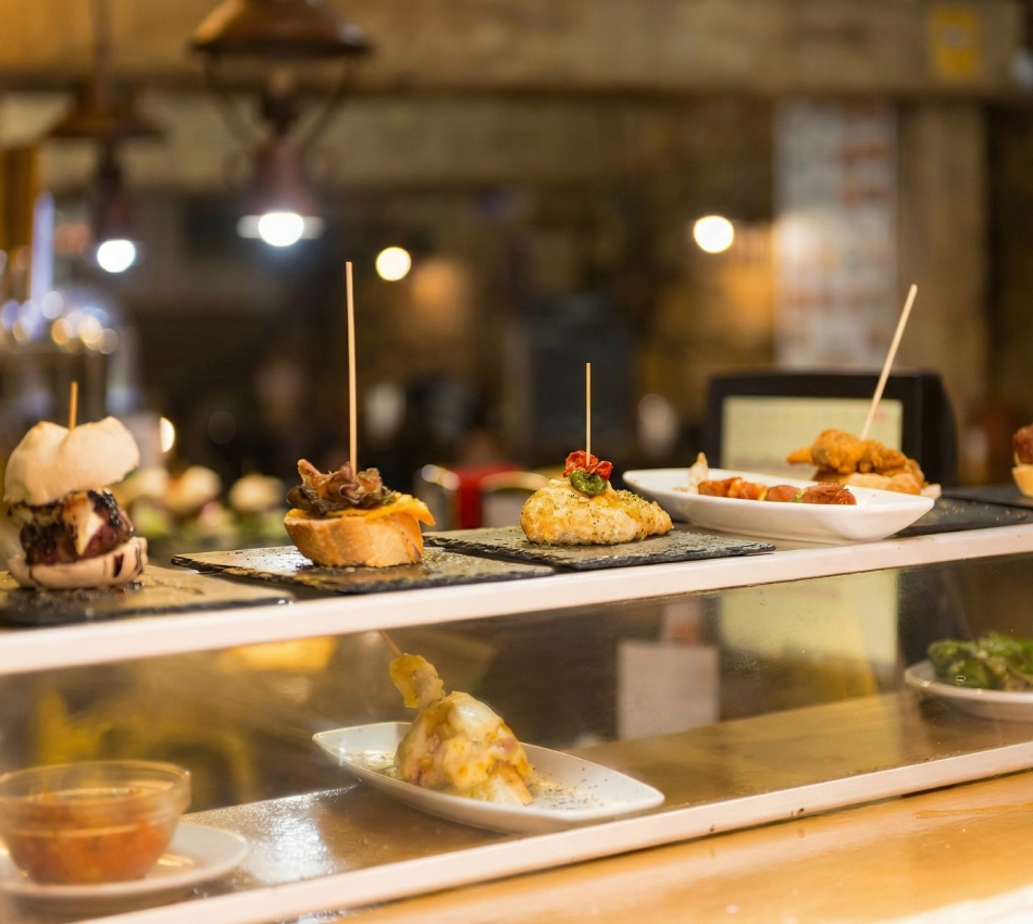 Tapas variadas en exhibici&oacute;n en un mostrador iluminado.