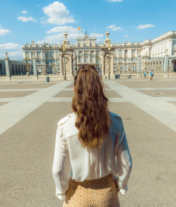 Mujer de espaldas mirando el Palacio Real en un d&iacute;a soleado.