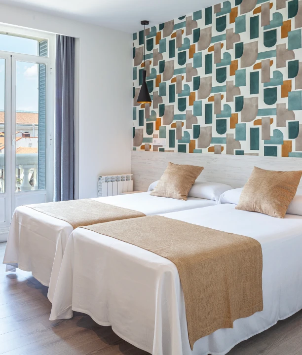 Habitaci&oacute;n con dos camas, decoraci&oacute;n geom&eacute;trica y ventana luminosa.