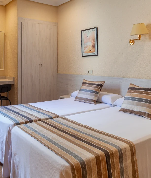 Habitaci&oacute;n de hotel con dos camas y decoraci&oacute;n en tonos neutros.