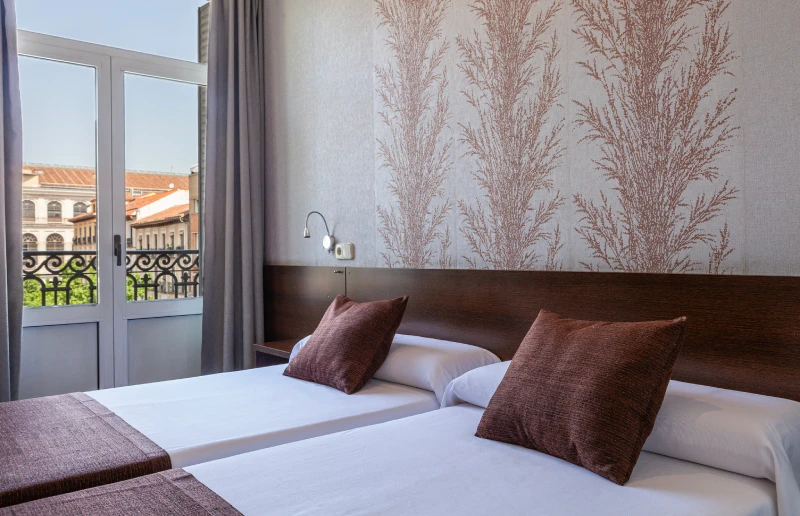 Habitaci&oacute;n moderna con dos camas y balc&oacute;n soleado.