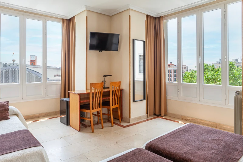 Habitaci&oacute;n luminosa con mesa, sillas, TV y ventana grande.