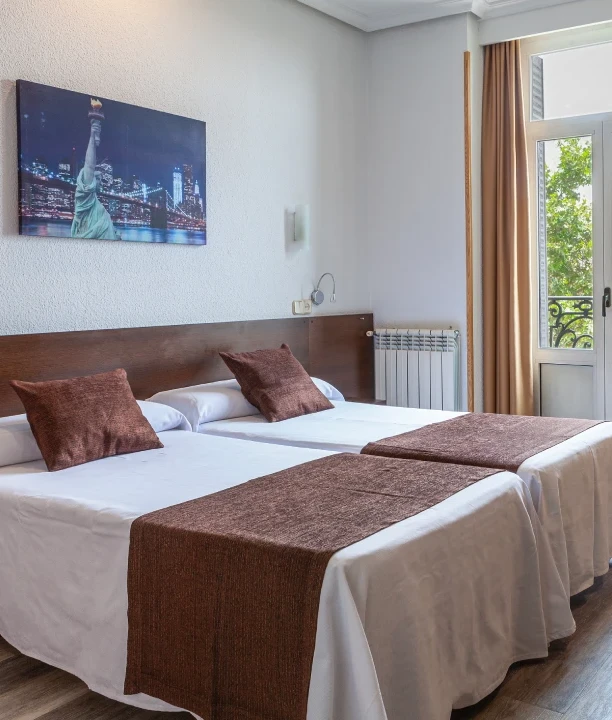 Habitaci&oacute;n de hotel con dos camas y decoraci&oacute;n urbana en la pared.