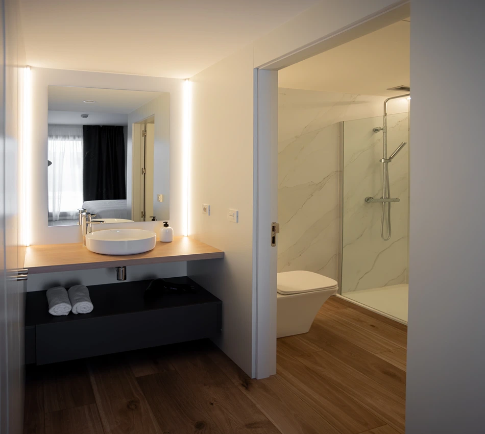 Ba&ntilde;o moderno con lavabo, espejo grande e iluminaci&oacute;n c&aacute;lida.