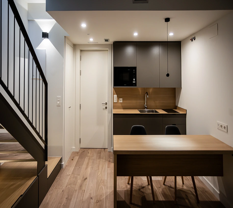 Cocina moderna y minimalista con escalera y mesa de madera.