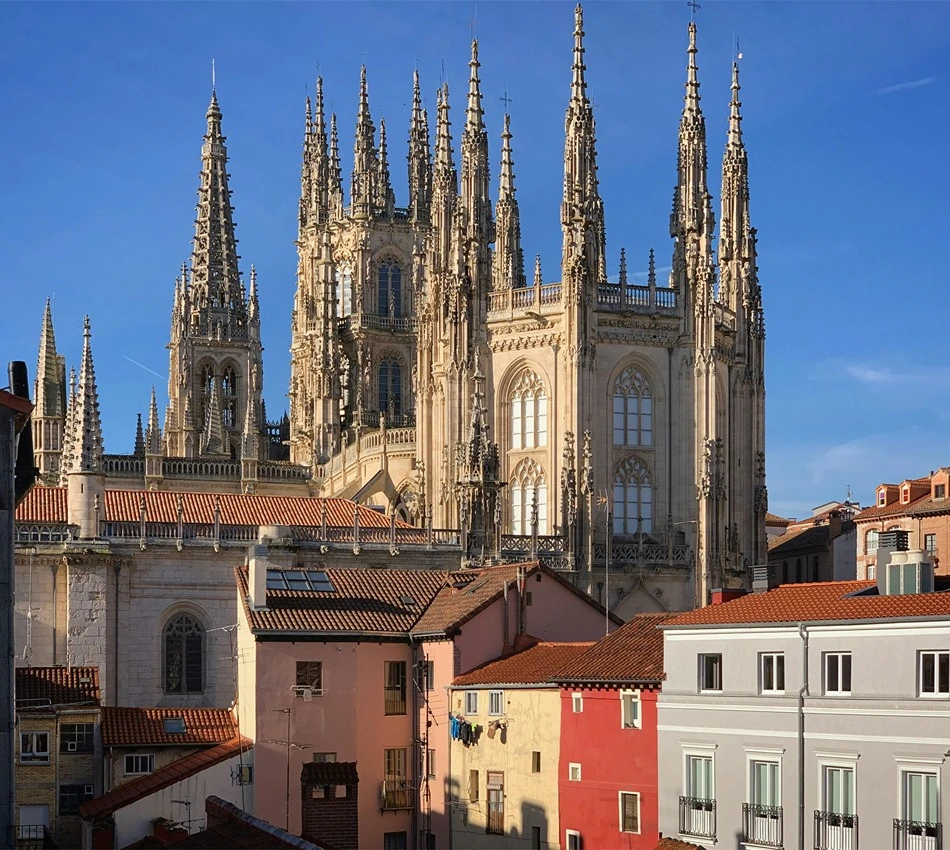Catedral g&oacute;tica con pin&aacute;culos detr&aacute;s de coloridas casas con techo de tejas rojas.