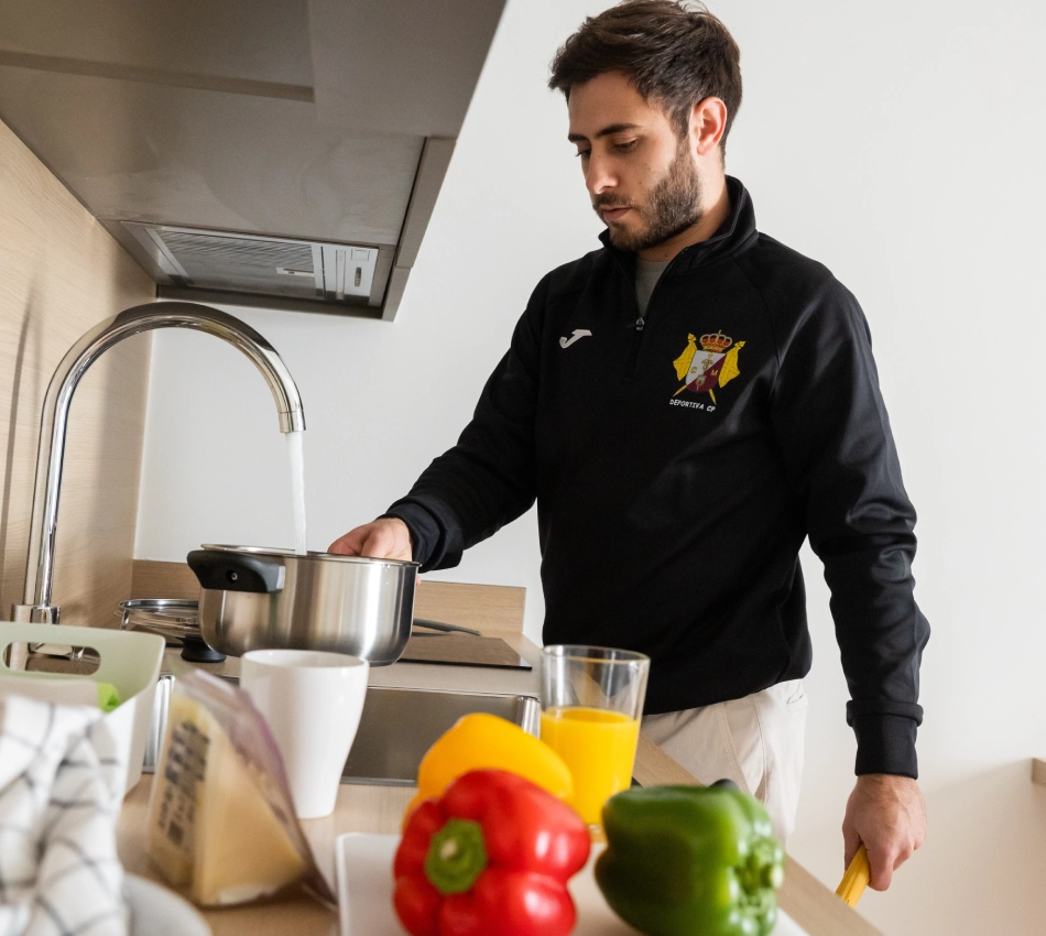 Hombre cocinando en la cocina junto a pimientos y jugo de naranja.