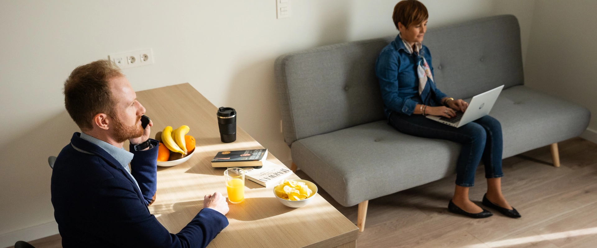 Hombre al tel&eacute;fono y mujer con laptop en una sala de descanso.