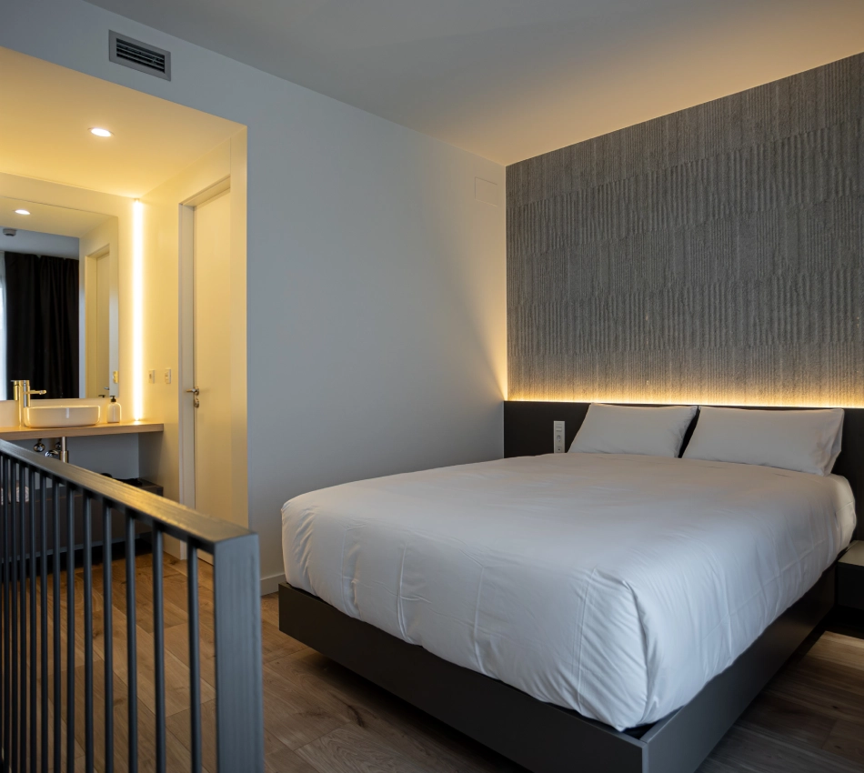 Dormitorio moderno con cama doble y ba&ntilde;o al fondo.