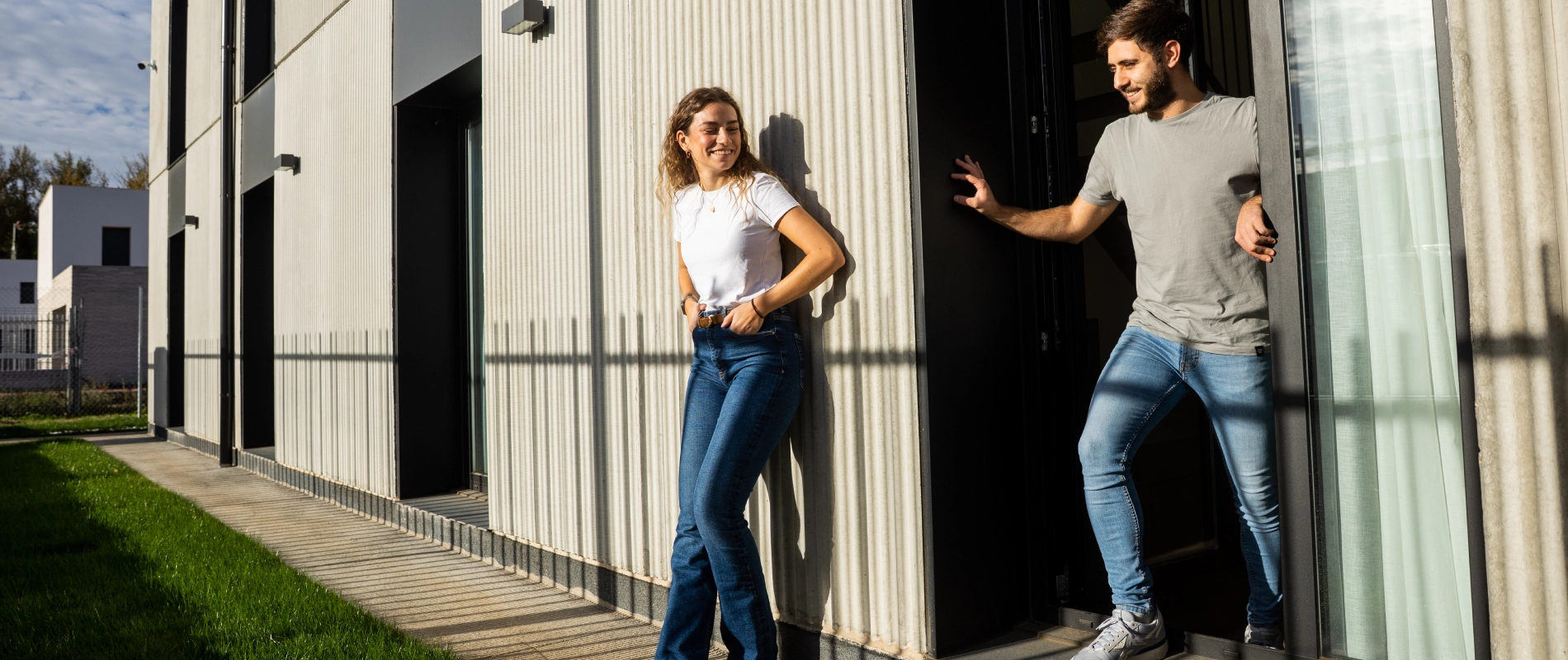 Dos personas sonr&iacute;en y salen de un edificio moderno en un d&iacute;a soleado.
