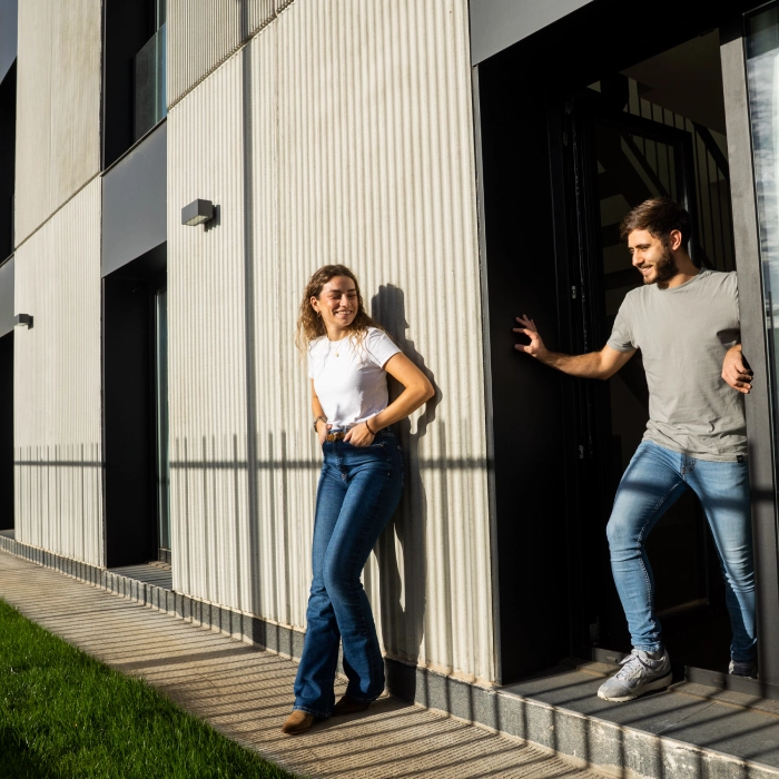Dos personas conversando afuera de un edificio moderno con sombra y sol.
