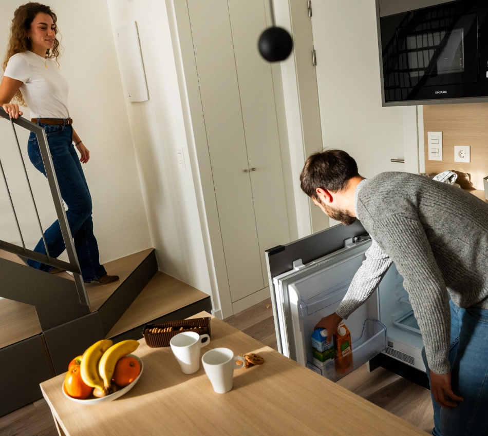 Hombre toma jugo del refrigerador mientras una mujer baja las escaleras.