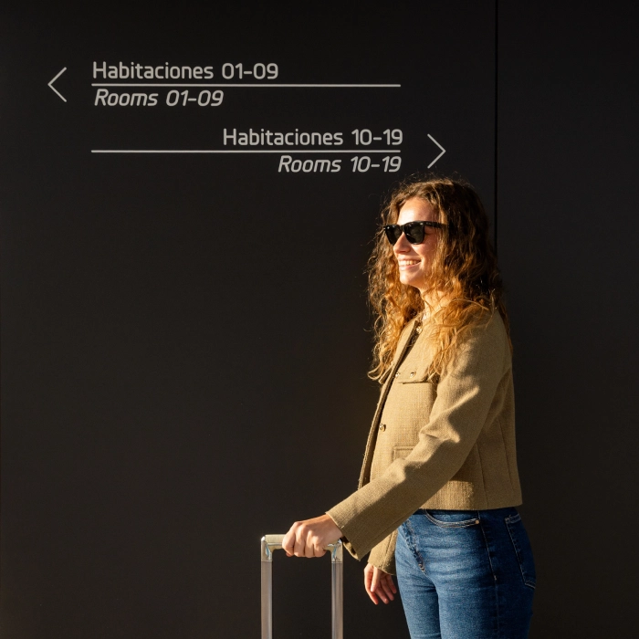 Mujer con gafas solares y maleta bajo se&ntilde;al de habitaciones de hotel.