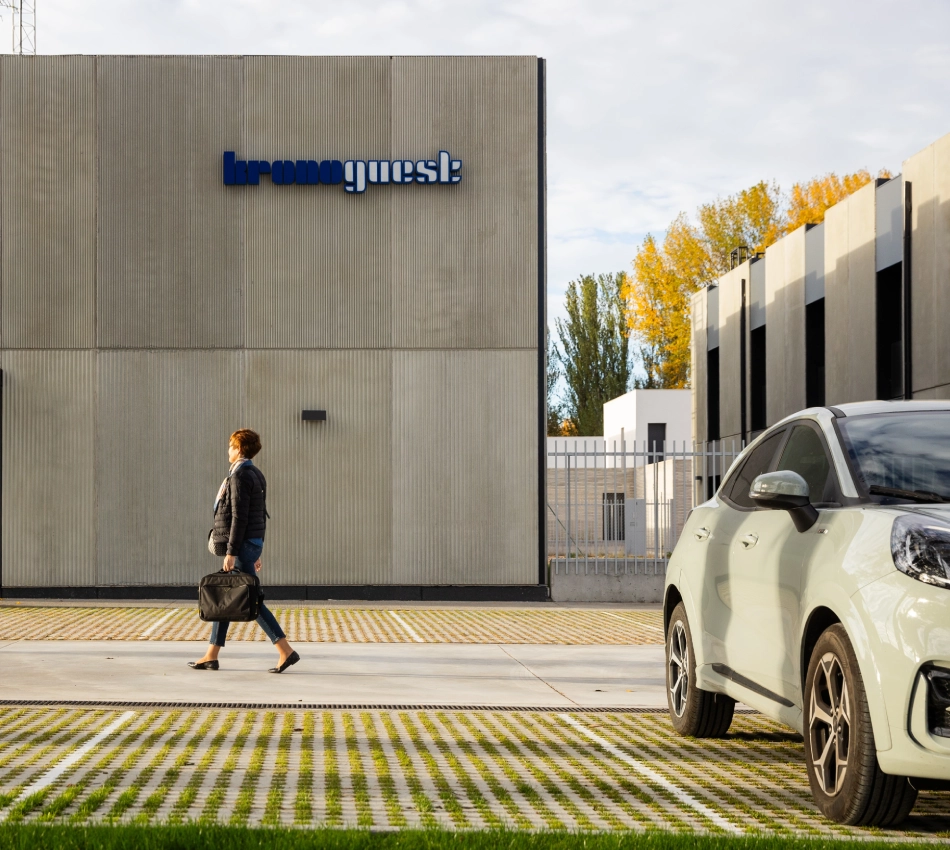 Mujer caminando frente a un edificio moderno junto a un auto estacionado.