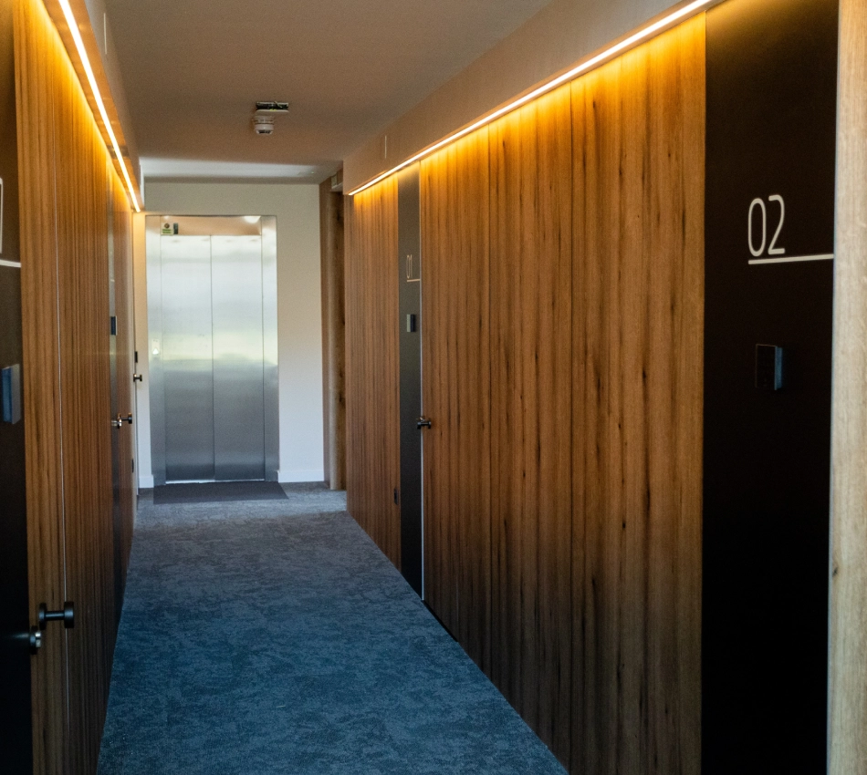 Pasillo moderno con puertas de madera y un ascensor al fondo.