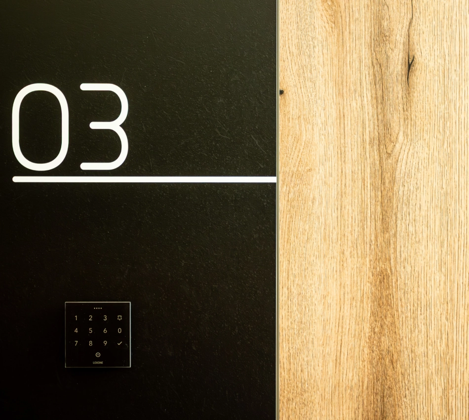 Panel negro con n&uacute;mero "03" y panel t&aacute;ctil num&eacute;rico, junto a madera clara.