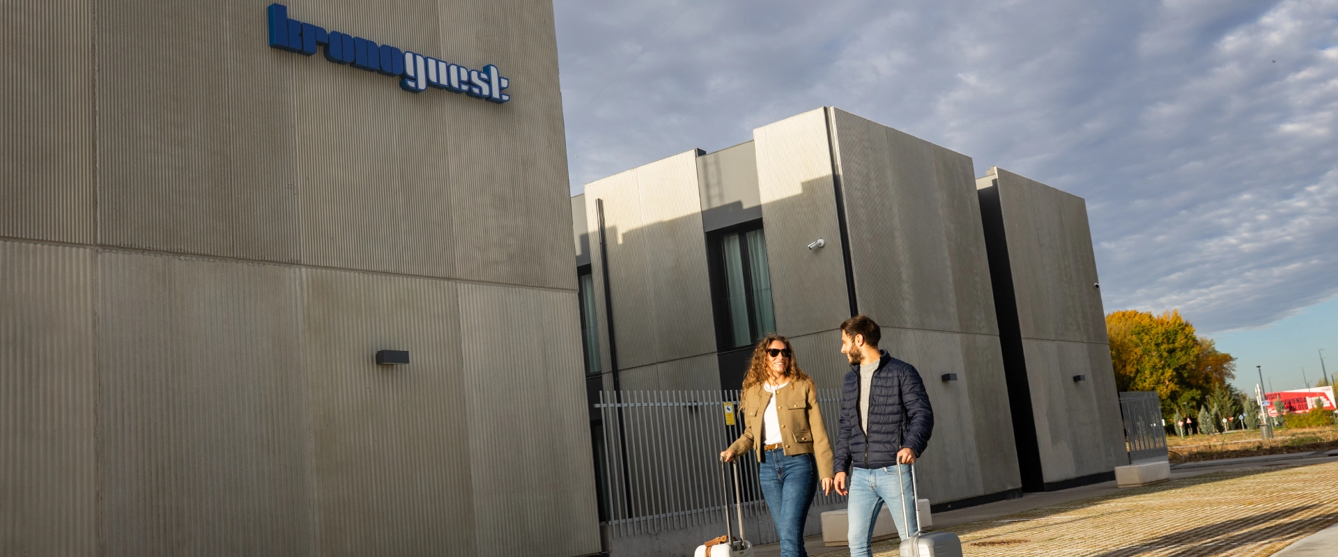 Personas con maletas caminando frente a un edificio moderno.