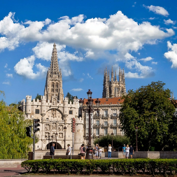 Catedral g&oacute;tica con cielo azul y nubes, personas caminando en primer plano.