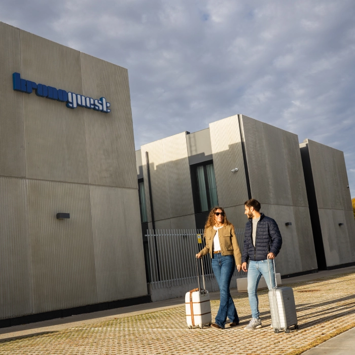 Pareja con maletas caminando frente a un edificio con el letrero "kronoguest".