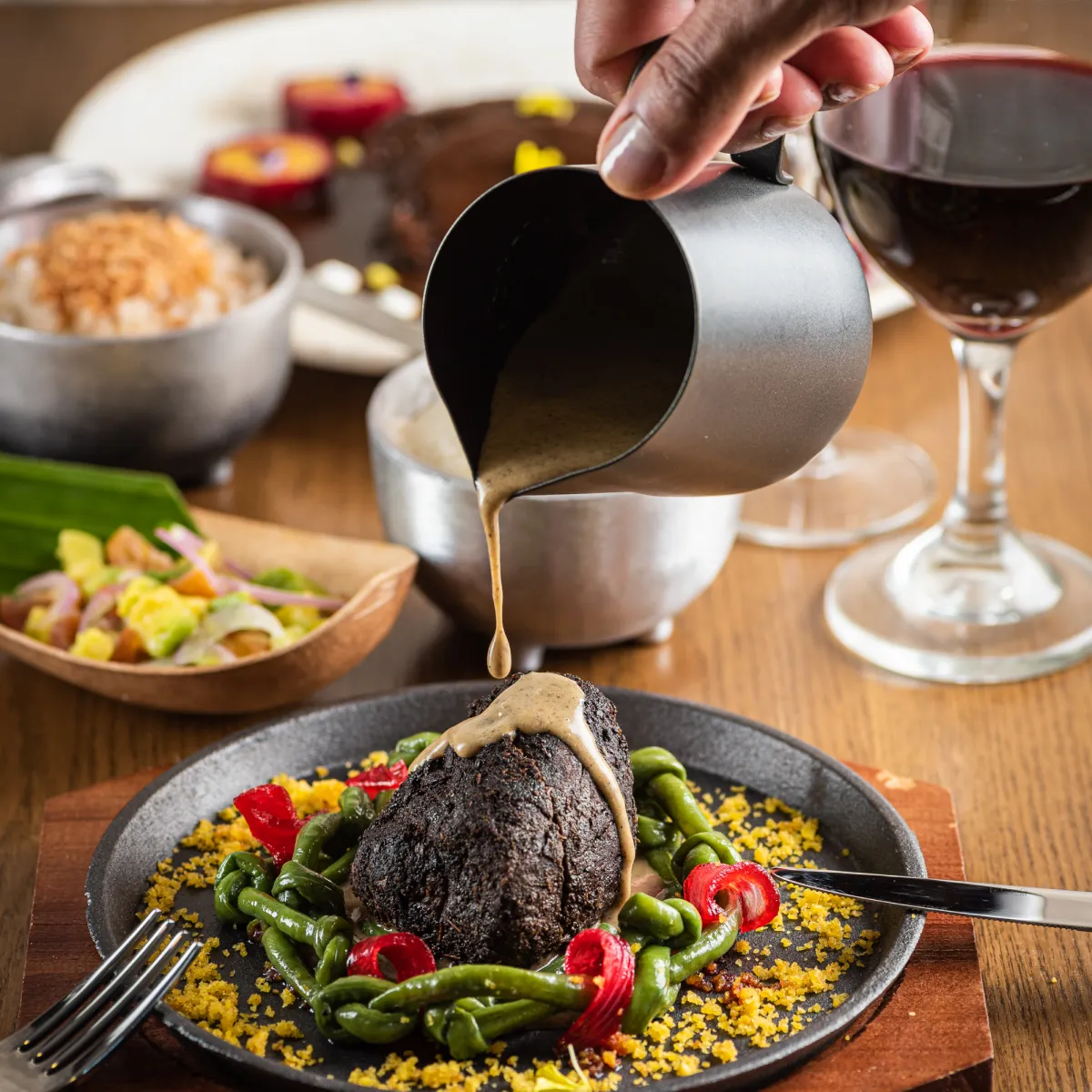Plato gourmet con salsa servida sobre carne y guarnición, junto a una copa de vino.